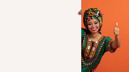 Cheerful black woman in african costume posing with advertising board