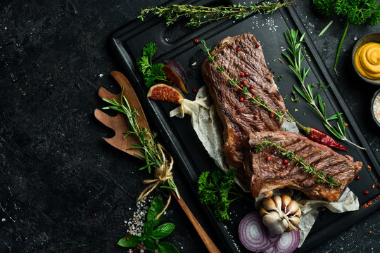 Barbecue. Grilled striploin steak with spices and rosemary. On a black concrete background. Free space for text.