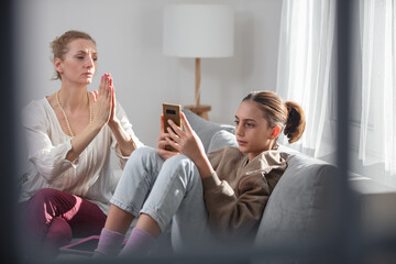 Mother having trouble with a lazy teenager girl at home while playing video games on a smartphone.