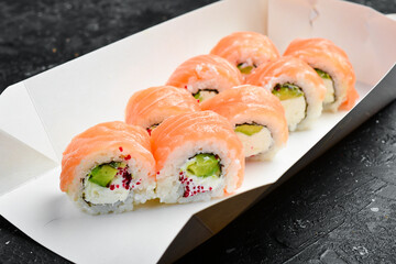 Sushi rolls with cheese and fish and caviar, Japanese food. Delivery. Disposable tableware. On a black stone background.