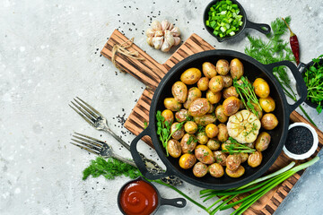 Roasted baby potatoes in an iron skillet on a gray stone background. Top view. Rustic style.