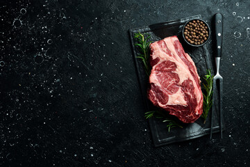 Raw marbled ribeye steak. Fresh meat and spices. Top view On a black stone background. Rustic style.
