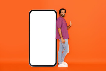 Stylish young hindu man posing by huge smartphone, mockup