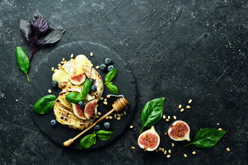 Naklejka na ściany i meble Baked brie cheese with figs, honey and blueberries. On a plate. On a black stone background.