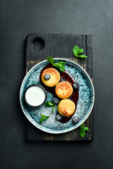 Cheese pancakes with blueberries and sour cream. Dessert. On a dark background, close-up.