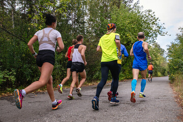 Fototapeta premium group runners male and female running race on park road rear view, autumn sports marathon