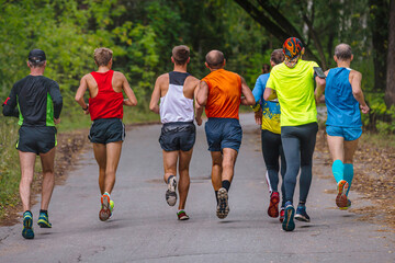 small group male runners run sports race on road in park, autumn marathon, fallen yellow leaves on ground