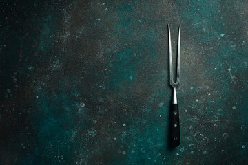 Metal fork for meat and steaks. On a dark green-turquoise background. Free space for text.