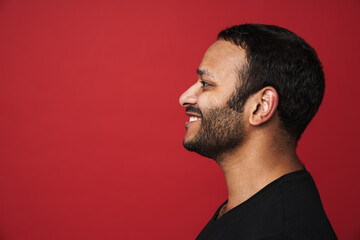 Profile of smiling indian man looking away isolated over red background