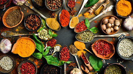 Colorful herbs and spices in spoons for cooking. Indian spices. On the background of black stone. Top view.
