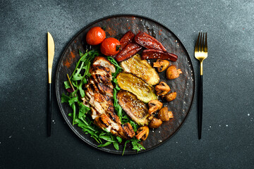 Grilled chicken fillet with grilled vegetables on a plate. Barbecue menu. On a dark background, close-up.
