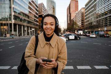 Fototapeta premium African girl listening music with headphones and smartphone while walking outdoors