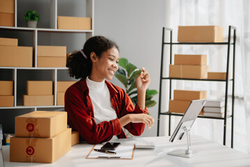 Young African woman prepare parcel box and standing check online orders for deliver to customer on tablet, laptop Shopping Online concept..