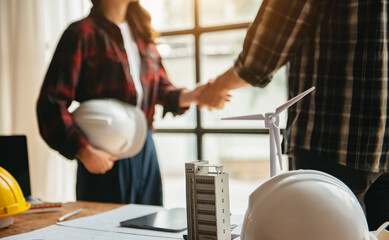 Engineers or architecture shaking hands at construction site for architectural project, holding safety helmet on their hands.
