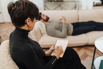 Female psychologist writing down notes during therapy session with man