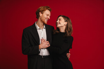 Beautiful couple looking at each other while standing isolated over red wall