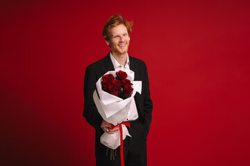 Cheerful man holding roses bouquet isolated over red wall