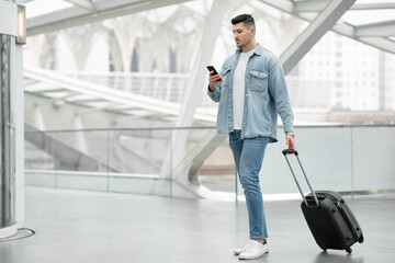 Fototapeta na wymiar Male Using Smartphone Texting Standing With Travel Suitcase In Airport