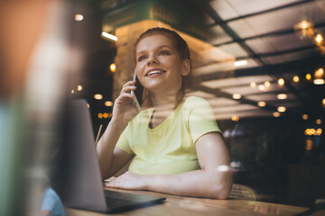 Cheerful woman speaking on smartphone in cafe
