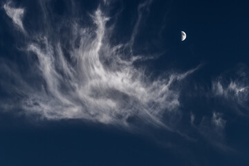 A crescent moon against a dark blue sky and a white cloud