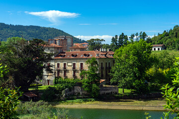 Fototapeta na wymiar old manor house on river bank against background of high-rise buildings. Spain, Basque Country