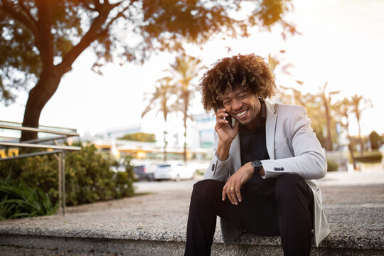 Excited african american middle aged businessman talking on smartphone, sitting outdoors after work day, copy space