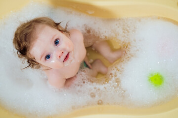 Baby girl in a bath with foam and soap bubbles. Happy laughing baby taking a bath playing with...