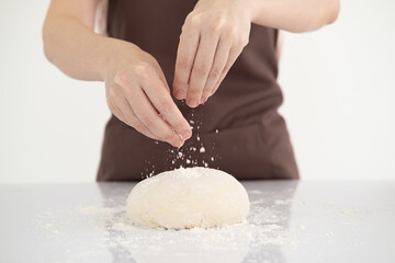 Woman sprinkling flour over fresh dough on white bright kitchen table.