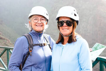 Senior women hikers with protective helmets standing on mountain enjoying a trekking day - Smiling climbing tourists enjoying holidays and healthy lifestyle - Freedom, success sport concept