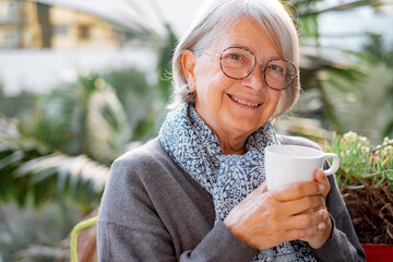 Portrait of happy senior woman smiling drinking hot coffee or tea standing outdoor on the home...
