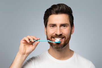 Morning procedure, oral care and perfect smile. Bearded man in white t-shirt holding toothbrush with paste and smiling