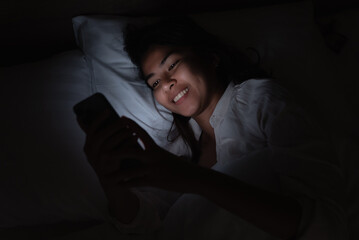 smiling woman using phone on bed at night - 591179951