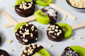 Kiwi Coved In Chocolate with Shredded Coconut and Nuts on a Stick, Healthy Snack on Bright Background