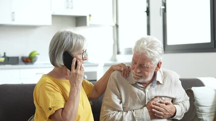 Mature woman, wife calling emergency, talking on phone, holding old husband hand, grey haired man having heart attack, touching chest, suffering from heartache disease at home, feeling pain
