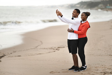 Smiling millennial african american family in sportswear in headphones take selfie on beach near ocean