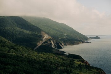 Aerial view of mountains covered with green forests against a sea on a foggy day