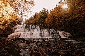 Scenic view of a waterfall flowing down the rocks in a forest on a sunny autumn day