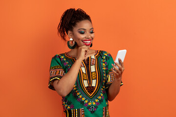 Stylish african woman in traditional costume using smartphone