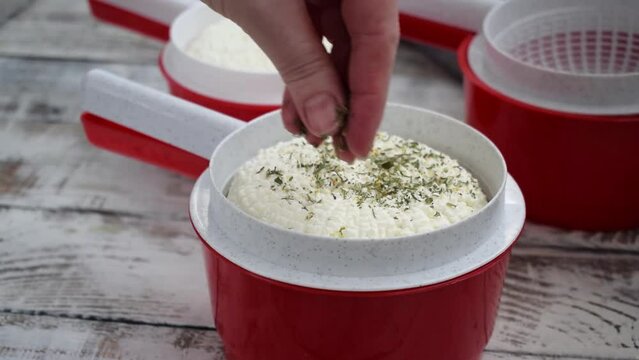 Making homemade adyghe cheese in the cheese making mold. Sprinkling the hot product with dried herbs and salt