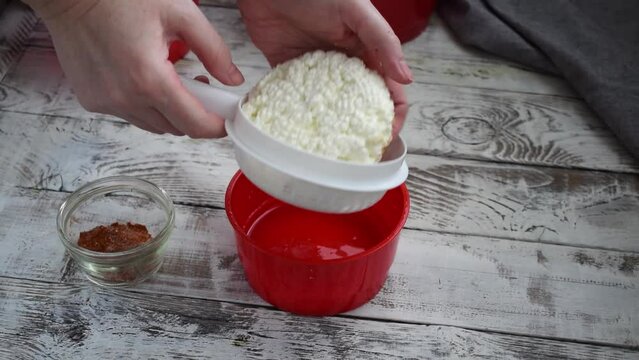 Making homemade adyghe cheese in the cheese making mold. Turning the hot product for further pressing and sprinkling the other side with smoked paprika 