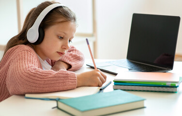 Smart focused serious teenager european girl in headphones doing homework with laptop