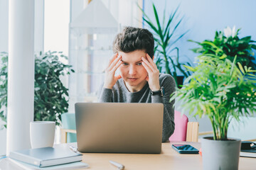 Middle aged shocked business woman sitting in front of laptop looking at screen at her workstation...