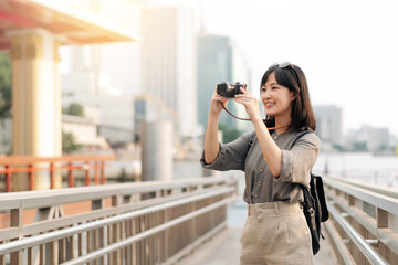 Young Asian woman backpack traveler using a camera in express boat pier on Chao Phraya River in...