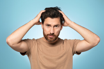 Fototapeta na wymiar Portrait of handsome bearded middle aged man looking at camera and touching his hair, posing over blue background