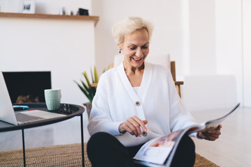 Cheerful senior woman reading magazine at home