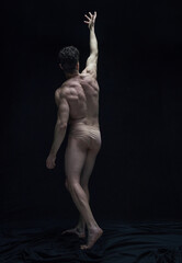 Relief body shape. Full-length portrait of handsome shirtless man posing in underwear against black studio background. Concept of male body aesthetics, men's beauty, inspiration, art