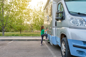 girl getting into a caravan parked next to a green area with grass and trees in the background