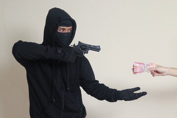 Portrait of mysterious man wearing black hoodie and mask doing shooting with gun while extorts...