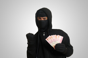 Portrait of mysterious man wearing black hoodie and mask stealing one hundred thousand rupiah...