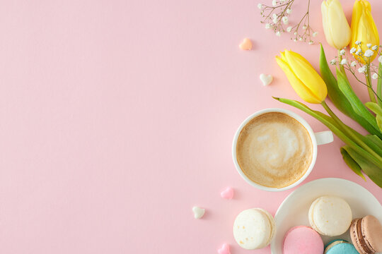 Mother's Day concept. Flat lay photo of cup of coffee plate with macaroons small hearts baubles bunch of colorful tulips and gypsophila flowers on pastel pink background with copyspace